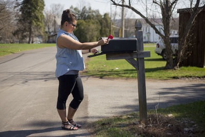 Side view of young woman standing by mailbox on street