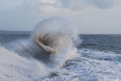 Sea waves splashing on shore against sky