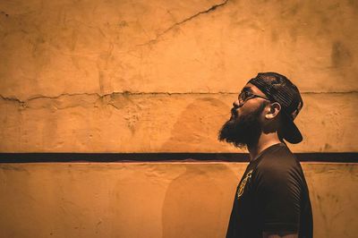 Side view of bearded hipster young man against wall at night