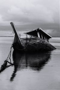 Abandoned ship in sea against cloudy sky