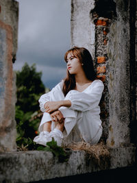 Young woman looking away while standing against white wall