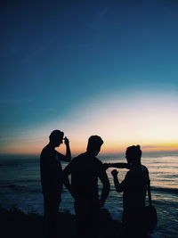 Silhouette friends on beach against sky during sunset