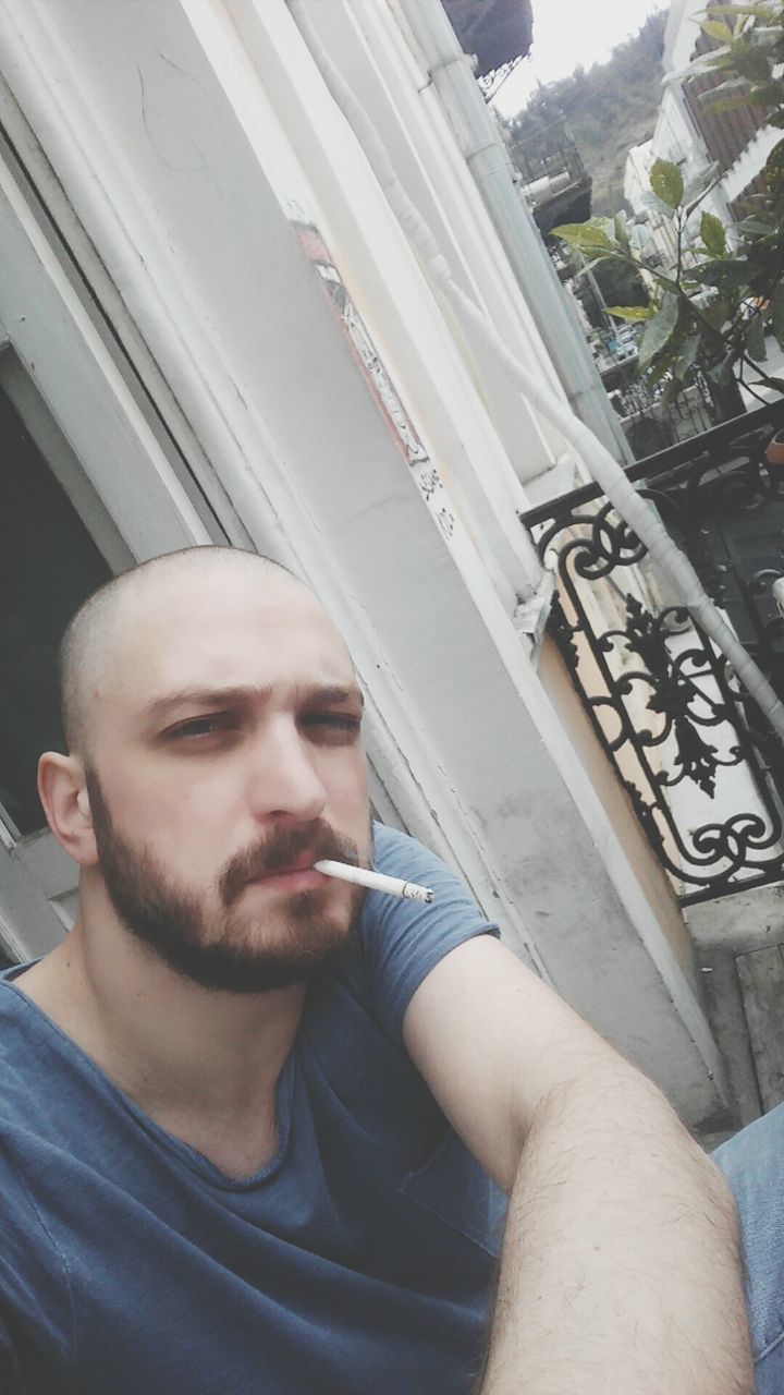 PORTRAIT OF YOUNG MAN SMOKING CIGARETTE ON A STREET