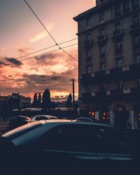 Cars on city street against sky during sunset