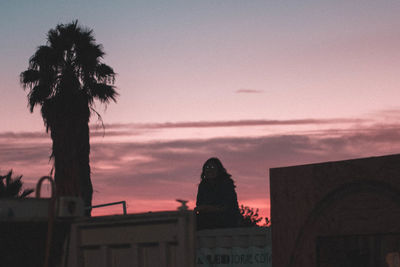 Silhouette palm trees by building against sky at sunset