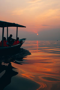 People in sea against sky during sunset