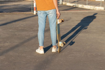 Cropped view of young man holding long board on his hands wearing an alternative street style outfit