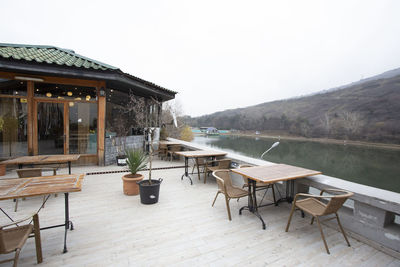 Empty chairs and table by lake against clear sky