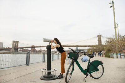 Woman using coin-operated binoculars while standing on promenade