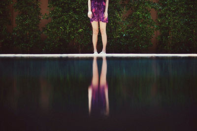 Low section of woman standing by swimming pool against trees