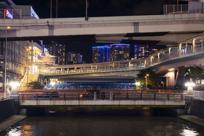 Illuminated bridge over river in city at night