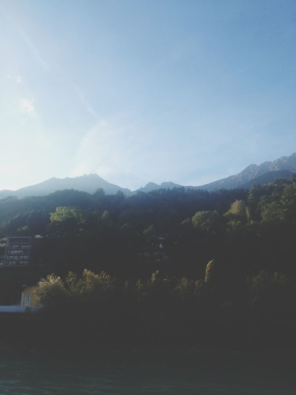 mountain, mountain range, tree, sky, water, tranquil scene, building exterior, built structure, scenics, tranquility, architecture, beauty in nature, nature, clear sky, copy space, blue, river, landscape, day, lake