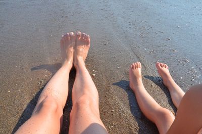 Low section of woman relaxing with child at beach