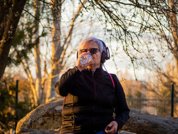 Senior woman drinking water from bottle in park during sunset