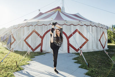 Female acrobat stretching while standing on one leg outside circus