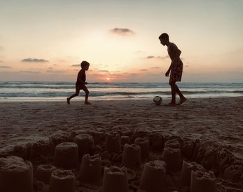 Full length of men playing at beach against sky during sunset