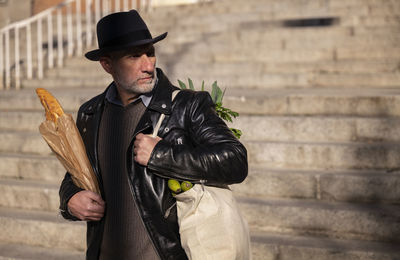 Adult man in hat holding bread and vegetable bag on street. madrid, spain