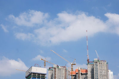 Low angle view of crane and buildings against sky