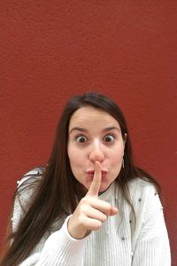 Portrait of beautiful young woman with finger on lips against wall