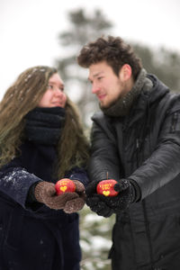 Young couple holding apples with text while standing in forest during winter