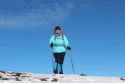 Woman with hiking poles standing in snow against blue sky