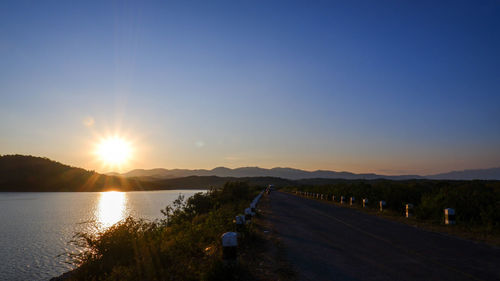 Road by lake against sky during sunset