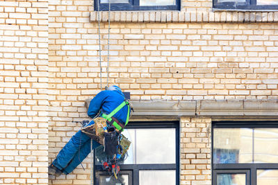 Builder climber hanging on safety ropes on the wall of an old building