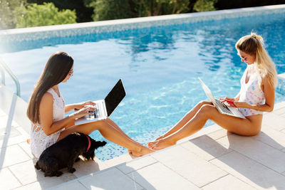 High angle view of women using laptop while sitting by swimming pool