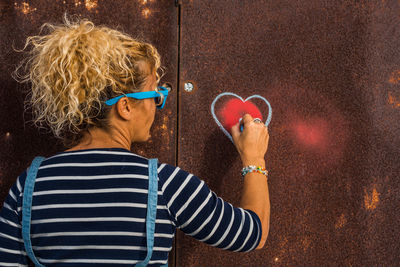 Rear view of woman making heart shape on rusty metal