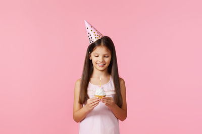 Portrait of young woman standing against pink background