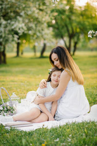 Mom hugs her daughter, sitting on a blanket in a spring blooming garden. maternal love