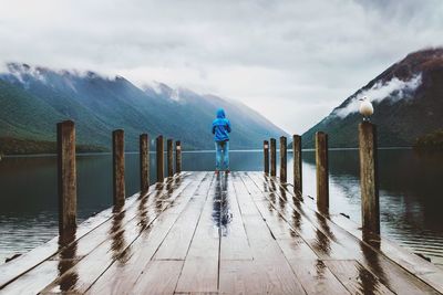 Rear view of person standing on pier over lake against mountain