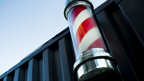 Low angle view of barbers pole on container against clear sky