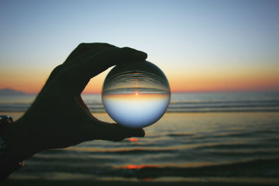 Closeup of a hand held glass ball on the beach during a sunset