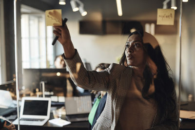 Mature businesswoman sticking adhesive note on glass wall in office