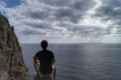 Rear view of man sitting on rock against sea at beach