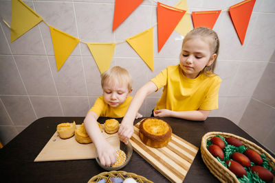 Children boy and girl prepare festive sweets decorate easter colored eggs on the table