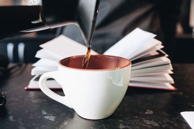 Close-up of jug pouring coffee in cup on table