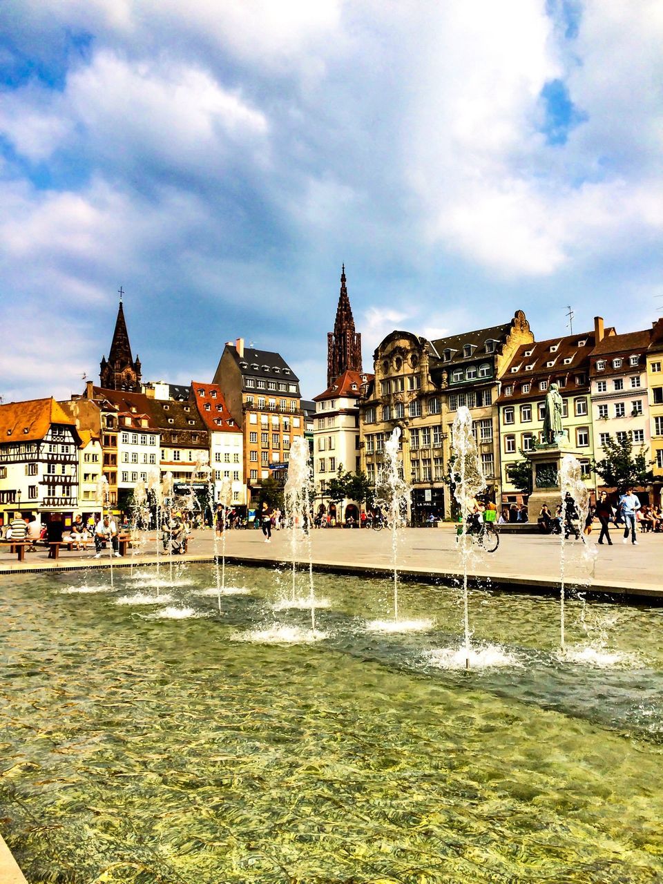 building exterior, architecture, built structure, sky, cloud - sky, city, incidental people, street, cloud, city life, water, residential building, large group of people, grass, residential structure, cloudy, building, travel destinations, outdoors, town square