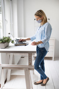 Side view of businesswoman wearing mask using laptop at home