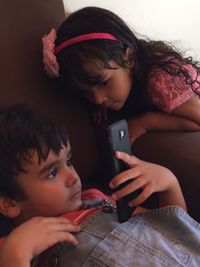 Girl looking at brother using smart phone while relaxing on sofa at home