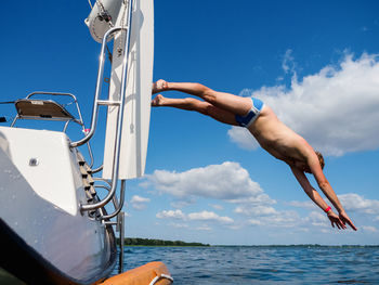 Young person jumping from a sailboat stern into the water, view from water person