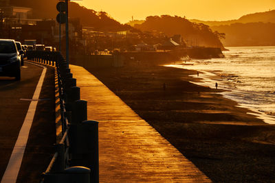 Traffic on the road by the beach and sea against sky at sunset