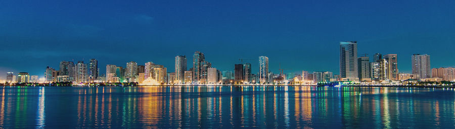 Illuminated city at waterfront against blue sky