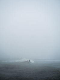 Person surfboarding on waves in sea against sky