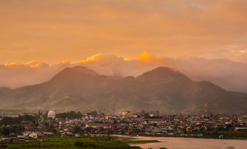 Scenic view of townscape by mountains against sky during sunset