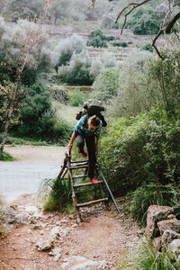 Young woman on wooden ladder against trees