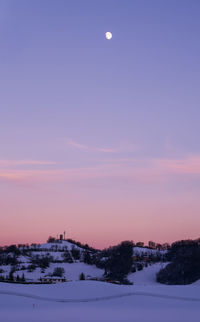 Half moon over snow covered landscape against sky