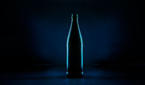 Close-up of illuminated bottle on table against black background