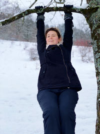 Woman hanging from tree branch with snowy background